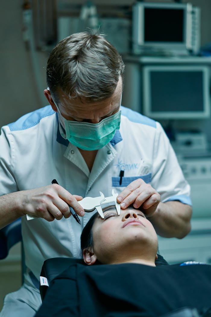 A surgeon measures a patient's eyelids with calipers in a medical clinic, preparing for a procedure.